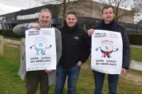 Drie mannen houden twee Boest-affiches vast met de slogan 'Samen scoren met Nederlands', voor de clubs Verbroedering Beersel-Drogenbos en Davoc Lot.